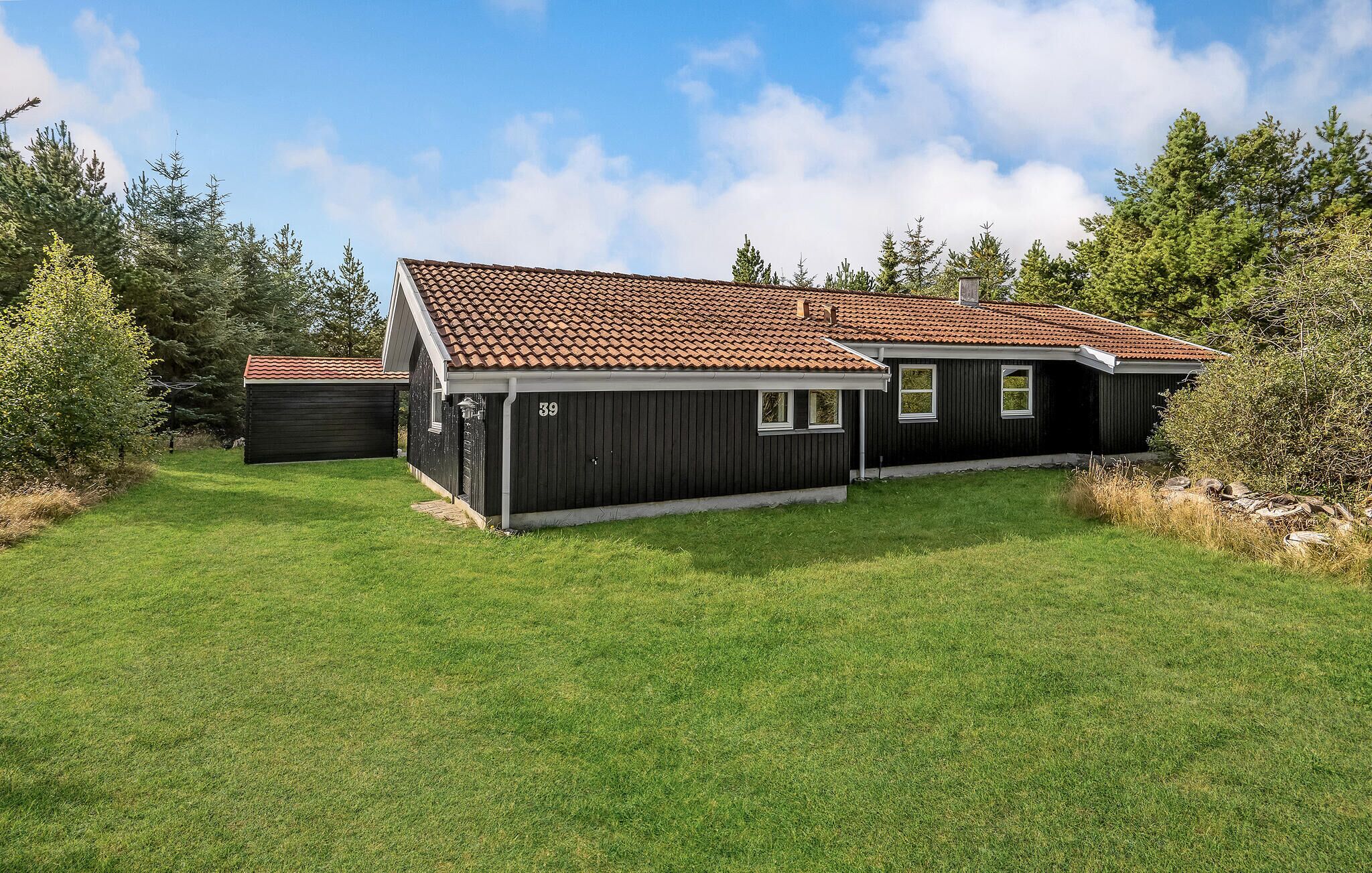 Une maison à deux étages, avec un toit recouvert de tuiles, le numéro « 39 » peint sur le côté et une pelouse bien entretenue.