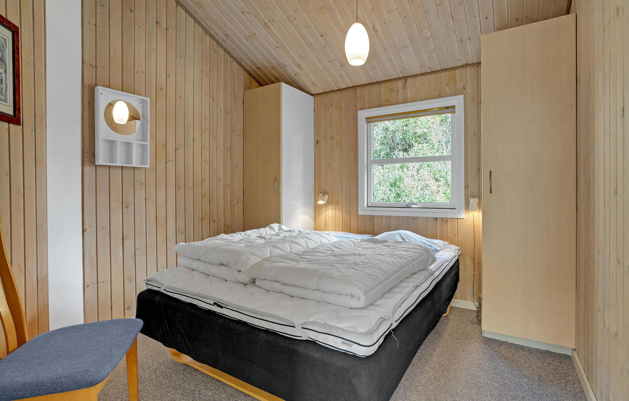 Ein Schlafzimmer mit einem Bett, einem Fenster, Holzwänden und einer Deckenleuchte.