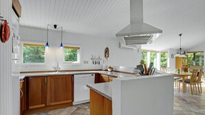 A modern kitchen with white cabinetry, a wooden island, and a dining area with a view of the outdoors.