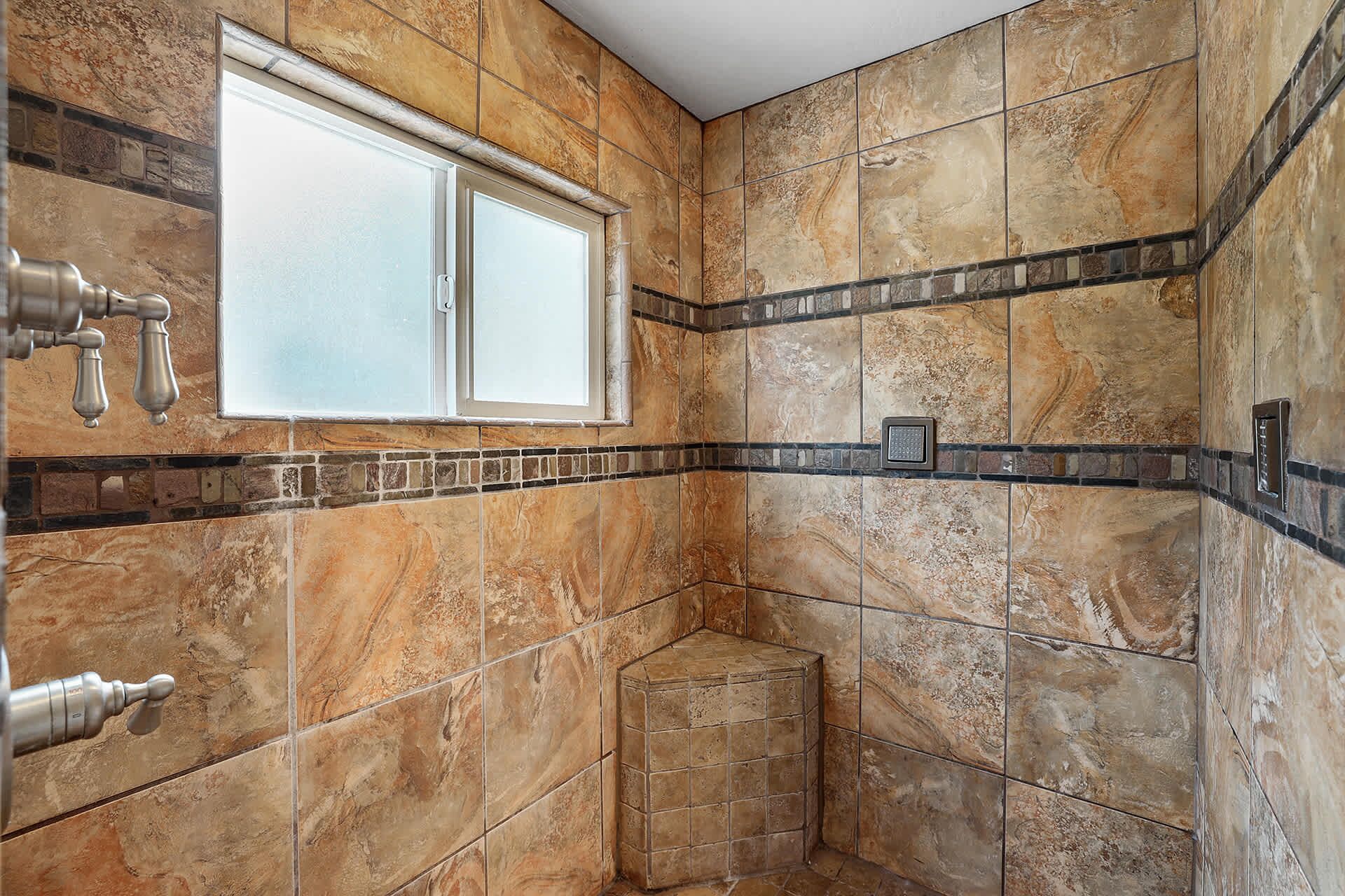 Une salle de bain avec une fenêtre, des murs carrelés et un espace douche d’angle.