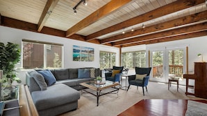 A spacious living room with a grey sectional sofa, a coffee table, and two armchairs. There are large windows and a wooden ceiling. - Hall Court Manor - Hot Tub, Pet Friendly, Pool Table! (Stateline)