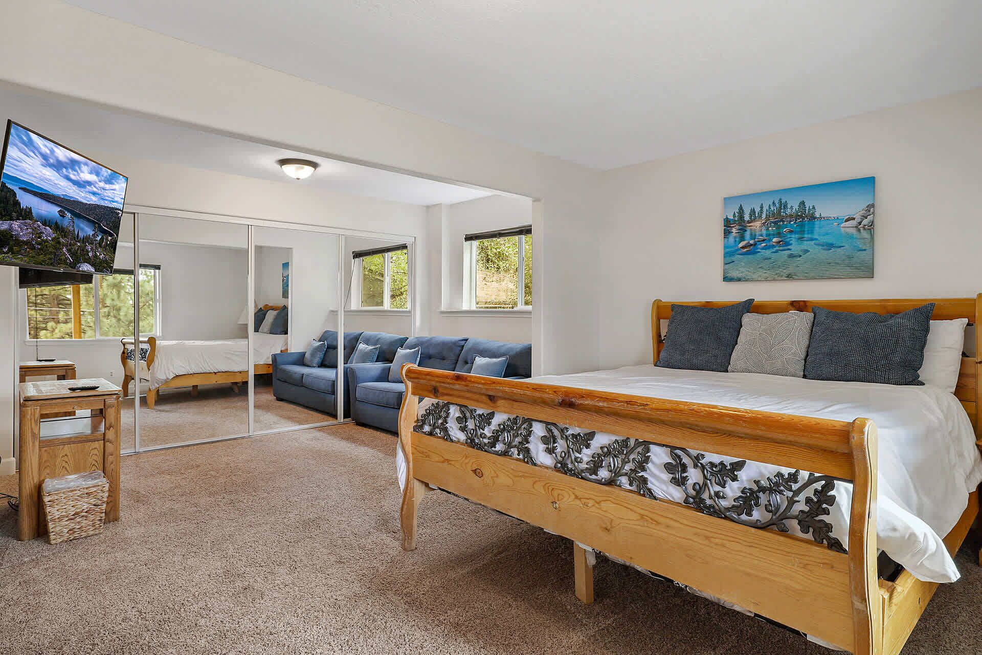 A bedroom with a wooden bed, a blue sofa, and a TV mounted on the wall.