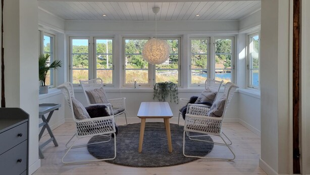 A bright room with large windows, wicker chairs, a small table, and a hanging light fixture.