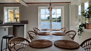 A dining area with a view of a lake, wicker chairs, and a central table with woven placemats.