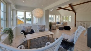 A spacious living area with wicker furniture, a wooden table, and large windows offering views of the outdoors.