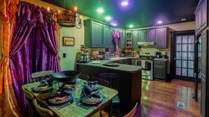 A kitchen with a dining area, featuring a wooden table set for a meal, a hanging light fixture, and green cabinets. - The Warlock House (Salem)