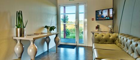 Un espace d’accueil comprenant un canapé, une table avec des plantes, un téléviseur et une porte donnant sur l’extérieur.