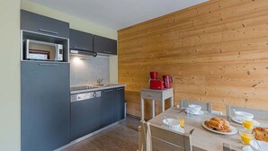 A compact kitchen with modern appliances, a wooden wall, and a dining area with breakfast items. - Centre-ville! Studio pour 4 + proche des remontées (Vaujany)