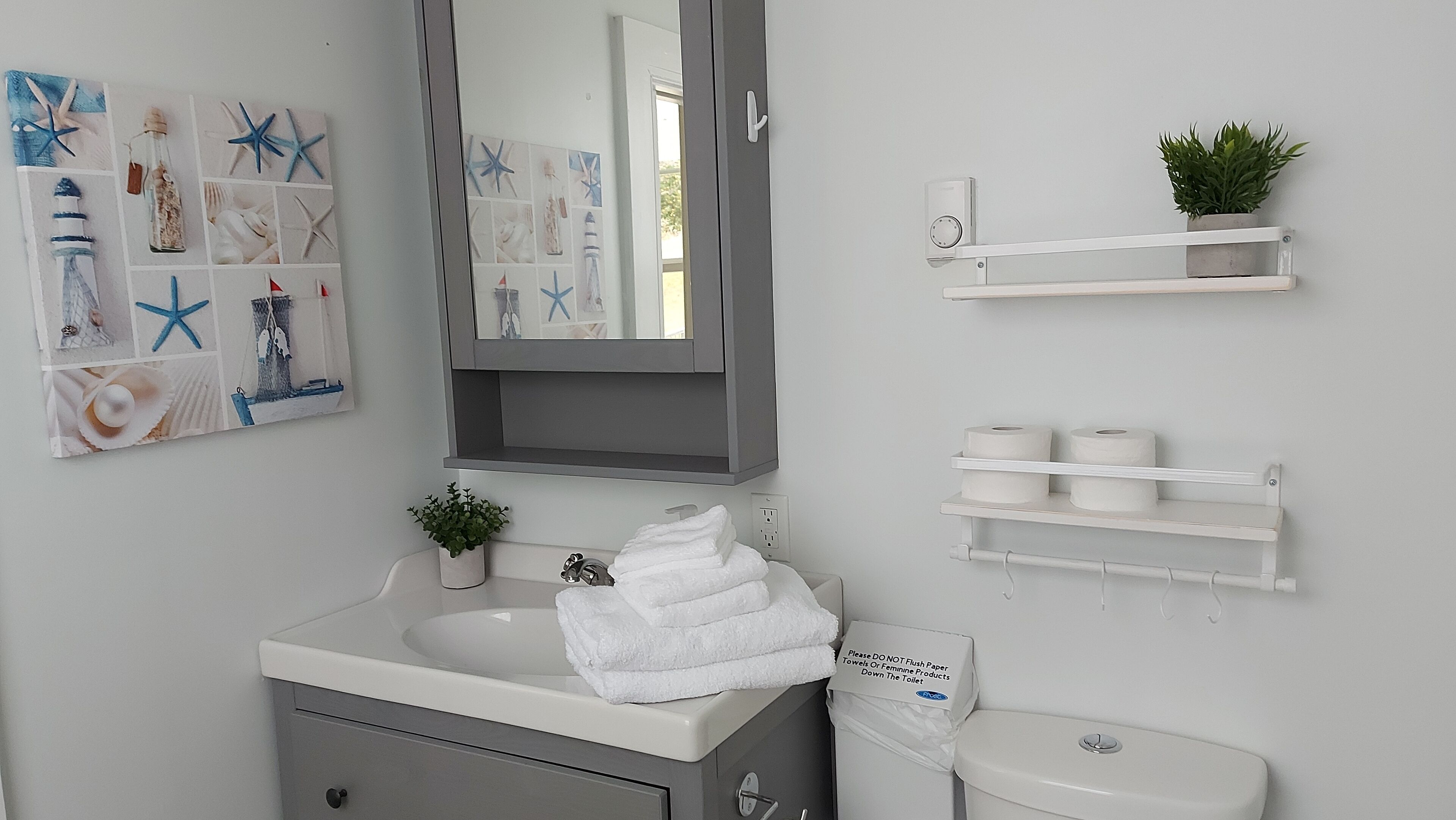 Ein Badezimmer mit Waschbecken, Spiegel, Handtuchhalter, Toilette und Ablagefläche mit Toilettenpapier.