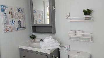 Ein Badezimmer mit Waschbecken, Spiegel, Handtuchhalter, Toilette und Ablagefläche mit Toilettenpapier.