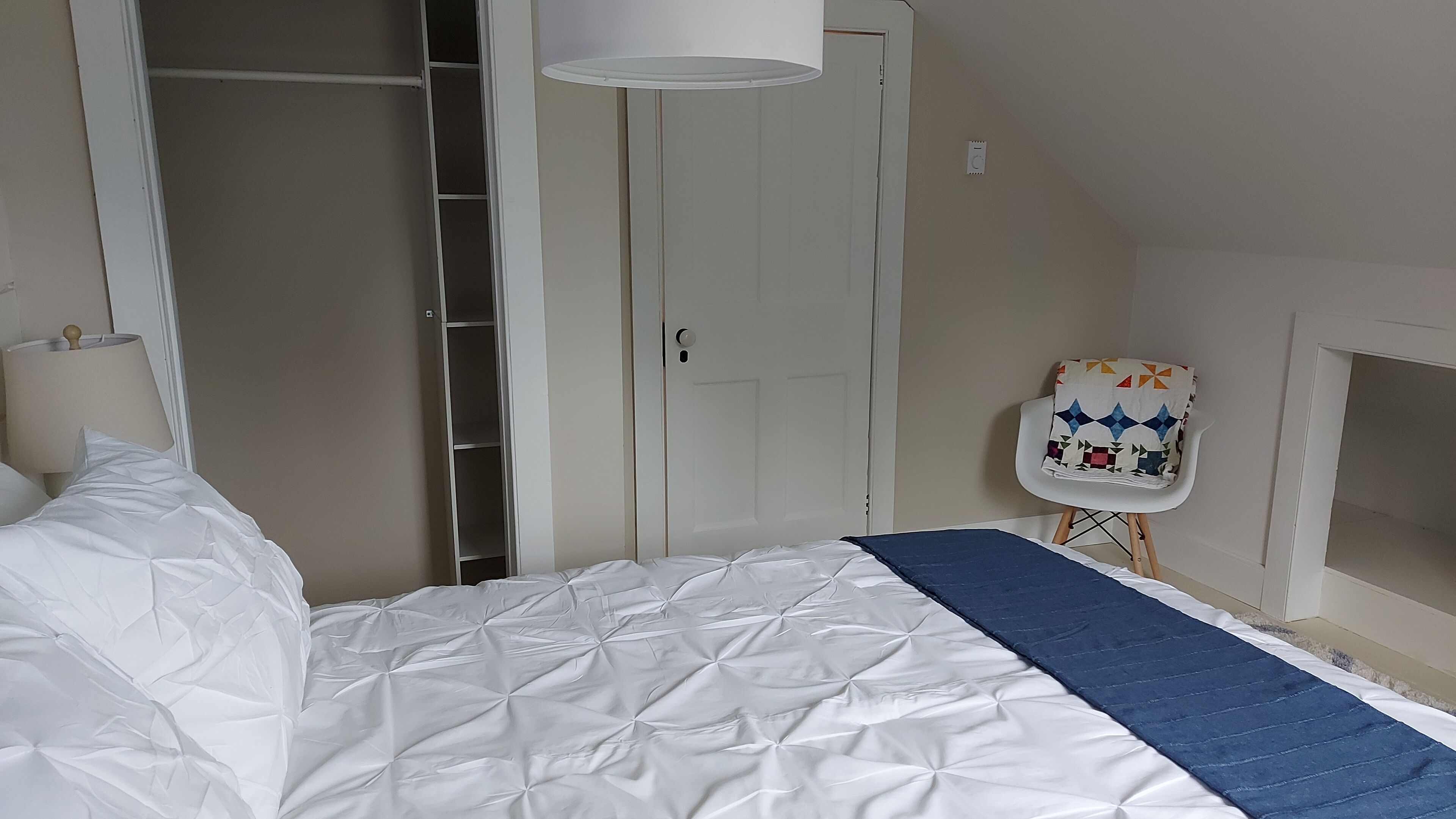 A bedroom with a bed, a wardrobe, a chair, and a lamp.