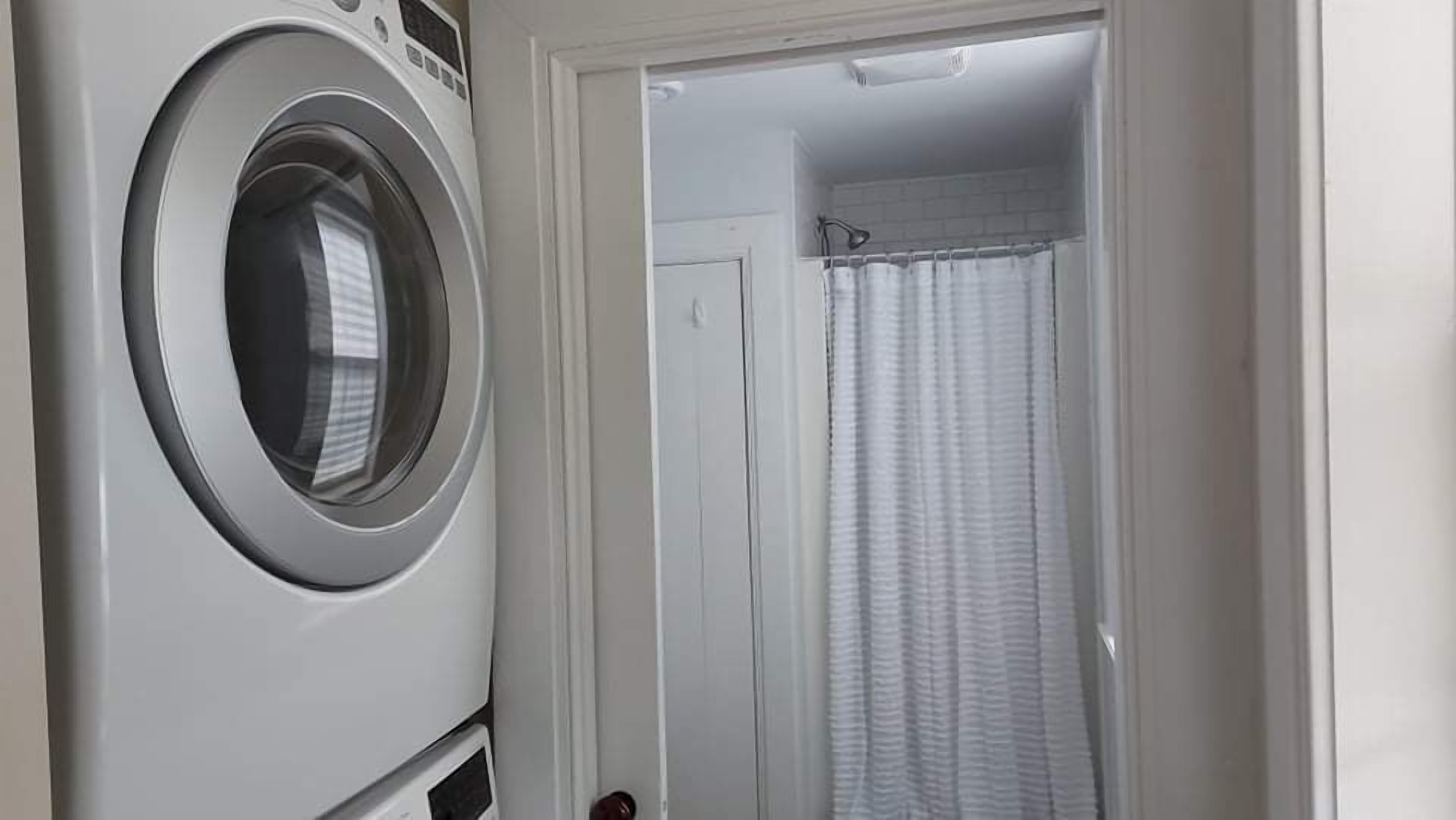 A laundry room with a front-loading washing machine and a shower area with a curtain.