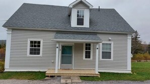 A single-story house with a front porch, a small entryway, and a garage door. - Cozy Harbour House - Scenic-relaxing-waterfront (Municipality of the District of Guysborough)