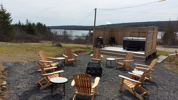 An outdoor seating area with Adirondack chairs and a fire pit, overlooking a lake. - Cozy Harbour House - Scenic-relaxing-waterfront (Municipality of the District of Guysborough)