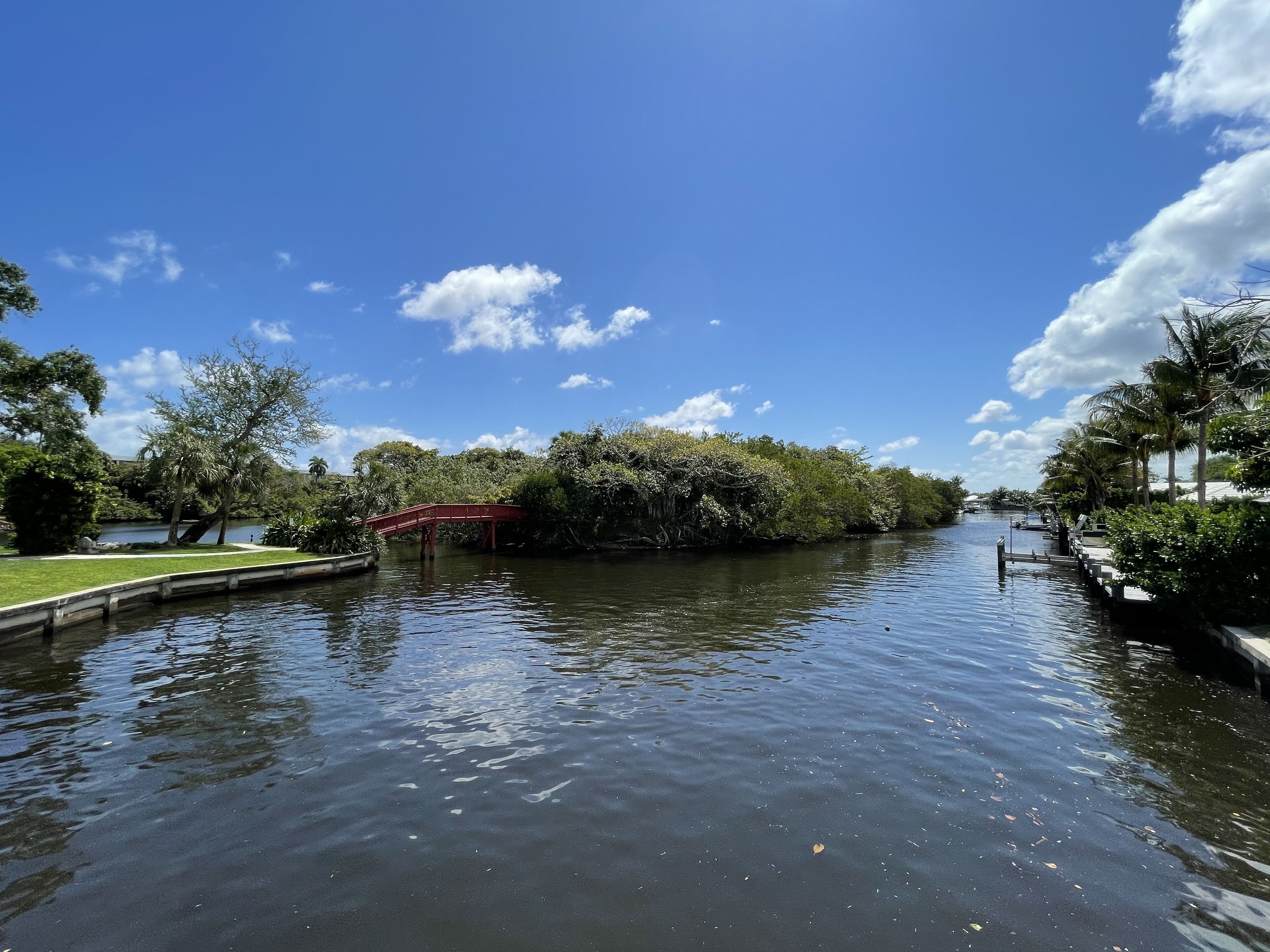 A calm waterway with a red bridge, surrounded by lush greenery and trees.