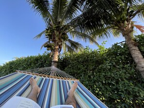 Eine Hängematte, die zwischen zwei Palmen gespannt ist, mit gestreifter Stoffbespannung. Eine Person liegt darin, und ein klarer, blauer Himmel ist zu sehen.