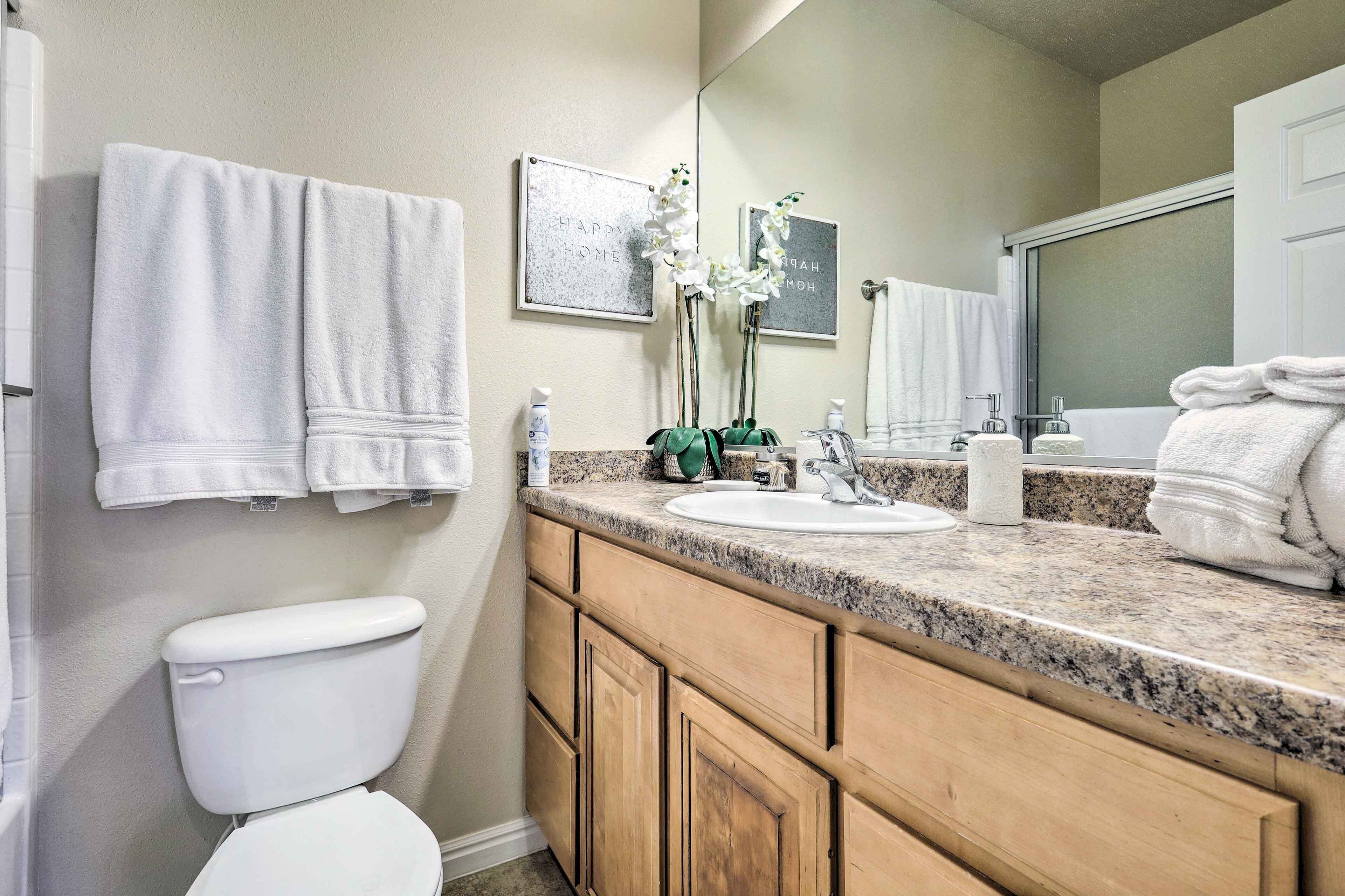 A bathroom with a toilet, sink, and mirror. There are towels hanging on the wall and a framed picture.