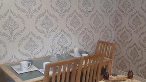 Uma área de refeições com uma mesa posta para dois, uma cadeira e papel de parede estampado.