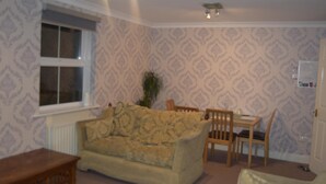 Uma sala de estar com papel de parede estampado, um sofá, uma mesa de madeira e uma cadeira.