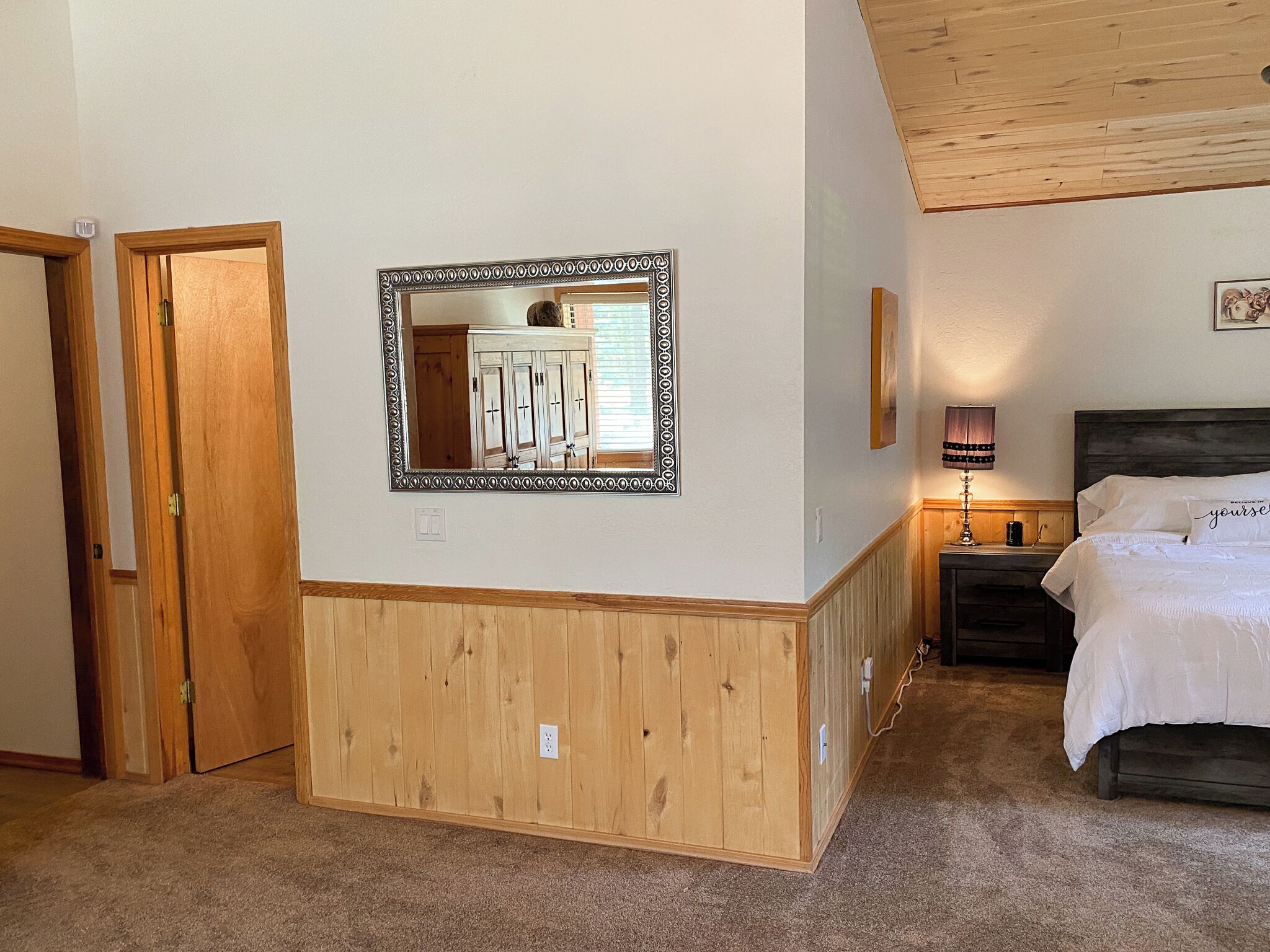 Ein Schlafzimmer mit einer Holzwand, einem Bett mit weißer Bettwäsche, einem Nachttisch mit einer Lampe und einem Spiegel an der Wand.