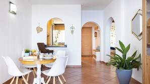 Un comedor con una mesa redonda de madera, sillas blancas y una planta en maceta.
