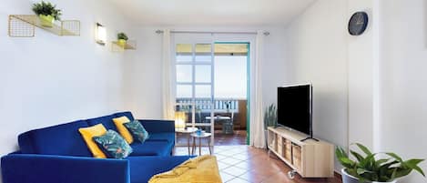 Ein Wohnzimmer mit einem blauen Sofa, einem Fernseher und einer Topfpflanze.