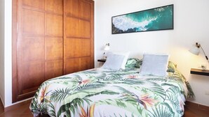 Un dormitorio con cama, armario de madera, un cuadro en la pared y mesita de noche con lámpara.
