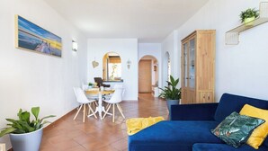 Una sala de estar moderna con un sofá azul, un comedor con sillas blancas y una cocina al fondo.