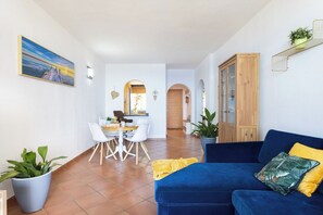 A living room with a blue sofa, a dining area with a table and chairs, and a kitchen in the background.