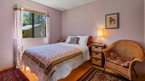Een slaapkamer met een bed, een rieten stoel, een nachtkastje, een lamp en een raam met gordijnen.