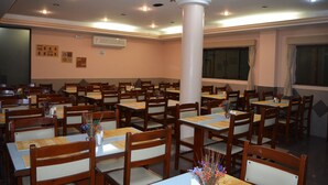Un área de comedor con varias mesas y sillas, una columna blanca en el centro y un ventanal amplio.