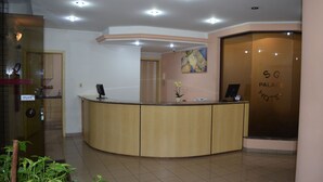 Zona de recepción de un hotel con un mostrador curvo, un cuadro en la pared y un letrero con el nombre del hotel.