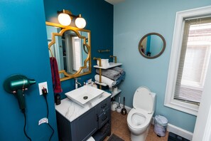 Een badkamer met een blauwe wand, een witte wastafel, een wastafelmeubel, een toilet en een föhn die in het stopcontact zit.