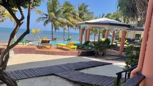 A beachside pool area with lounge chairs, a gazebo, and palm trees. - TBS 33 Beachside-Resort Style with Pool, 2 Bedroom (Placencia)