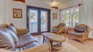 A spacious living area with wicker furniture, a large sliding glass door leading to a balcony, and framed artwork on the walls.