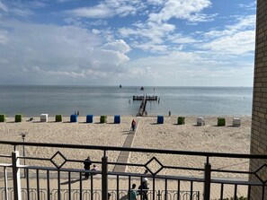 Una playa con un muelle que se adentra en el agua, cielo despejado y algunas personas en la arena.