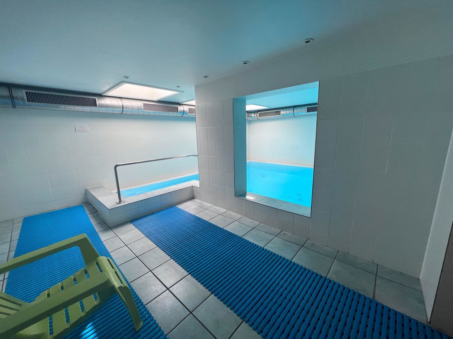 En swimmingpool med ett blått botten, en gul livräddarstol och ett fönster med utsikt över poolen.