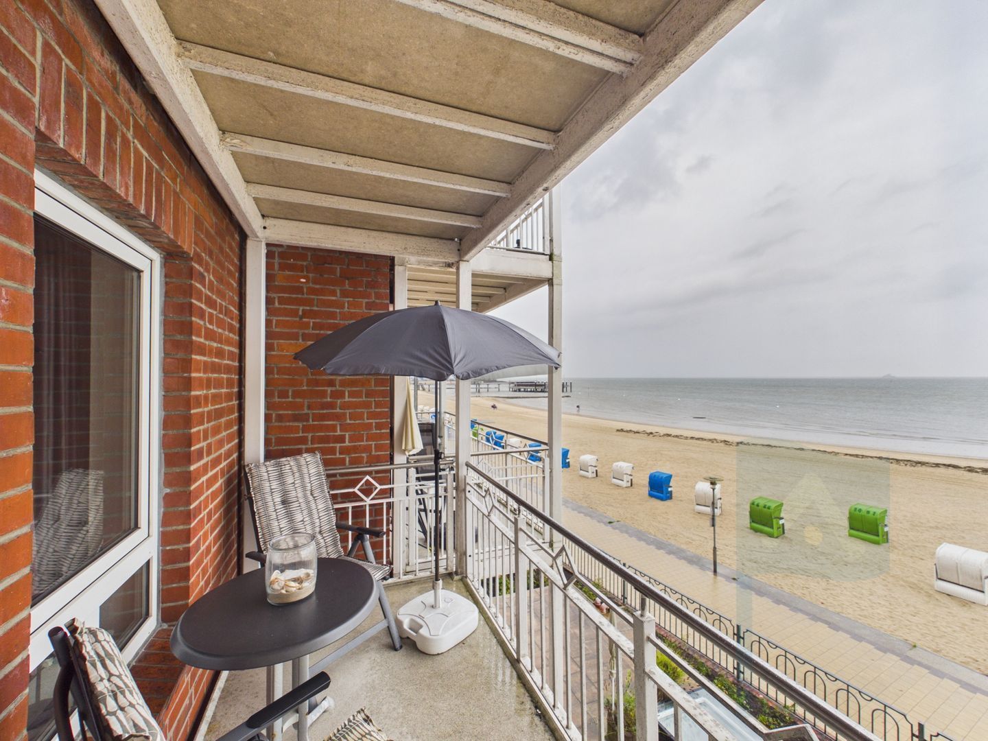 A balcony with a table, chairs, and an umbrella overlooking a beach.