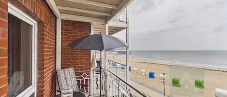 A balcony with a table, chairs, and an umbrella overlooking a beach.