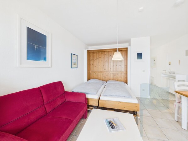 Quarto com sofá vermelho, cama com cabeceira de madeira, mesa branca e luminária pendente.