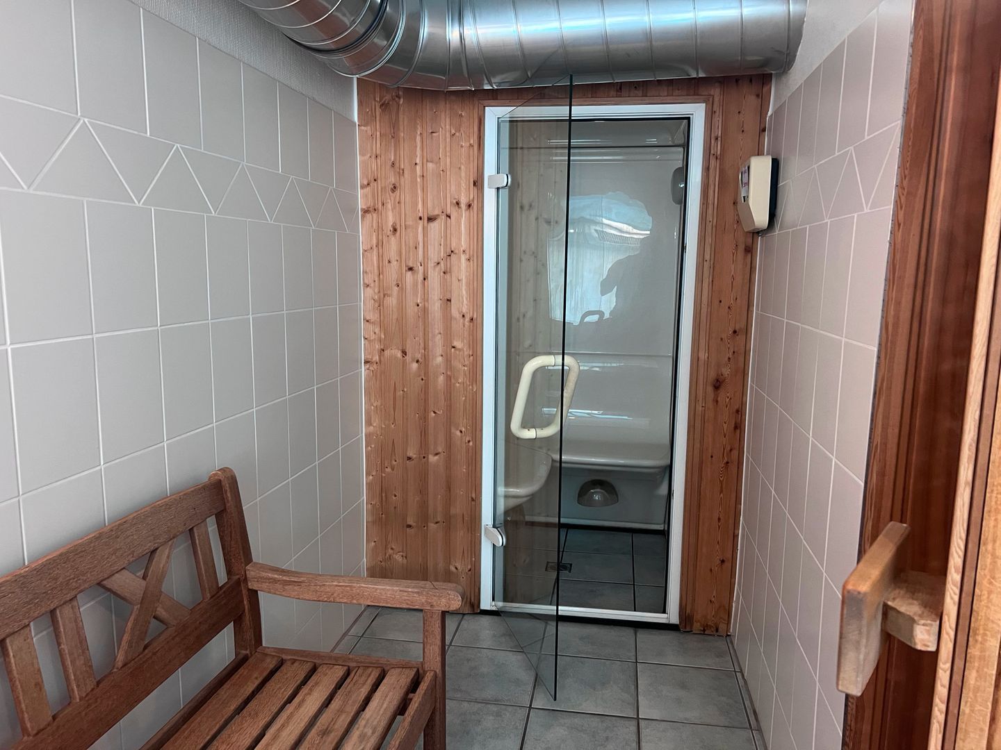 A small, enclosed bathroom with a wooden door, a bench, and a toilet.