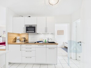 A modern kitchen with white cabinets, a built-in microwave, and a wooden countertop.