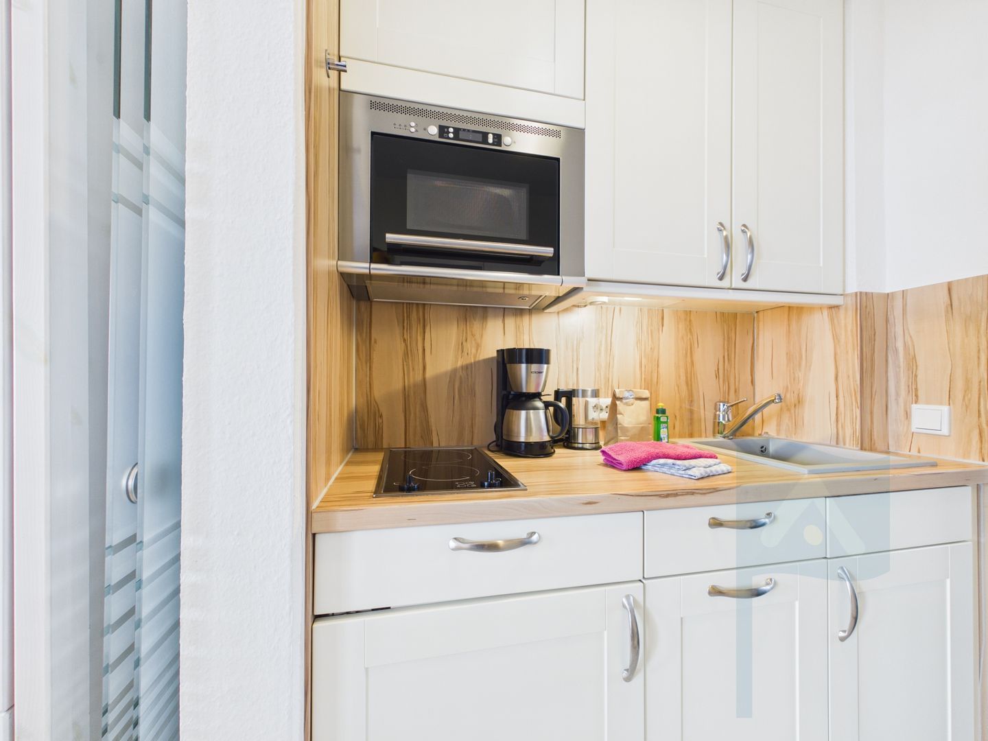 Una cocina compacta con microondas integrado, cafetera y lavamanos.