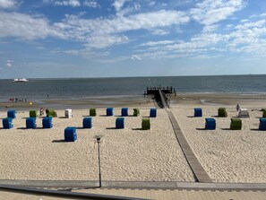 Une plage avec une jetée qui s’avance dans l’eau, des chaises de plage bleues et vertes, et un ciel dégagé.