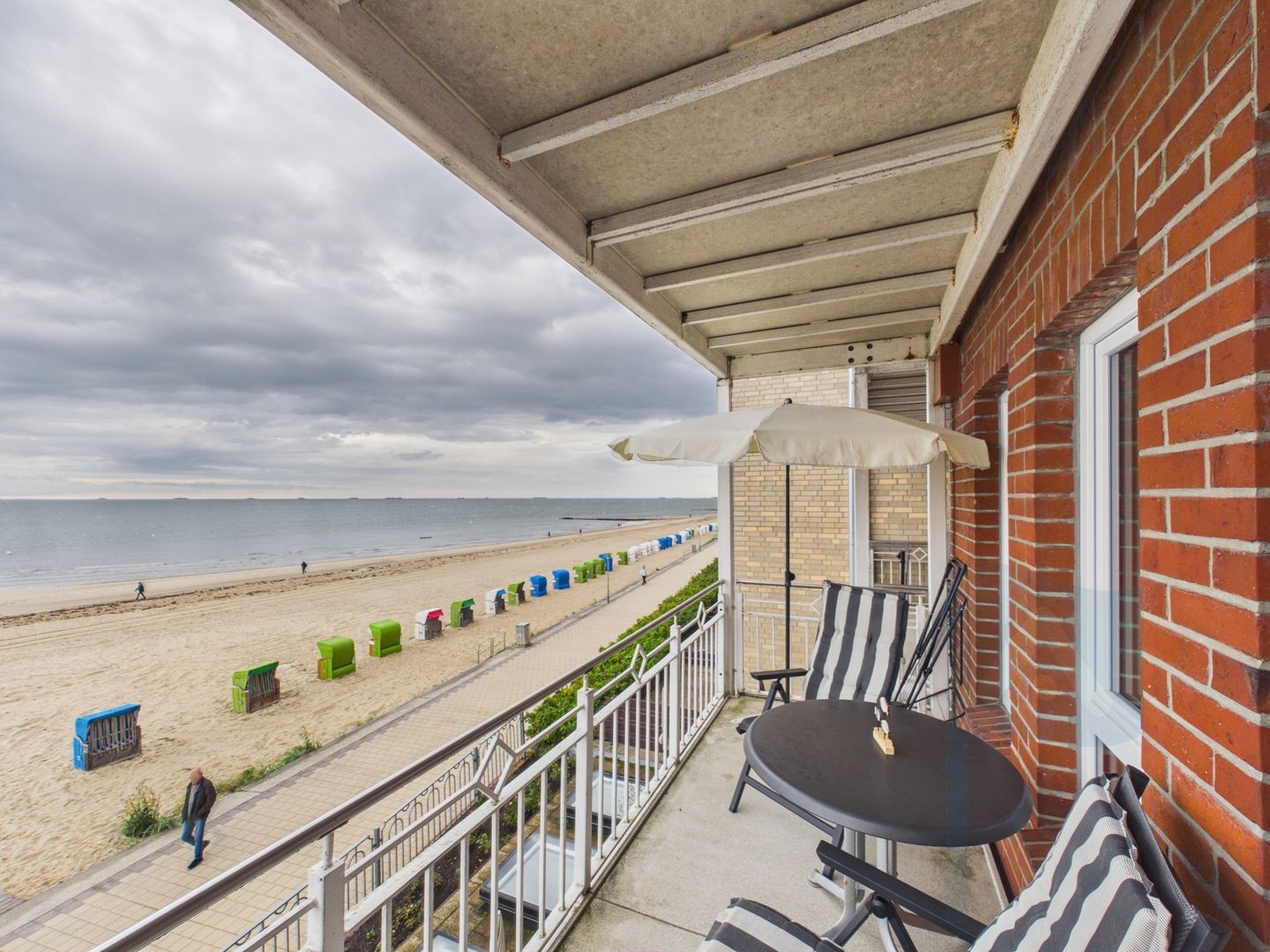 Een balkon met uitzicht op het strand, een tafel, stoelen en een afvalbak.