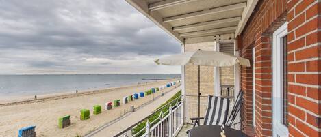 A balcony with a view of the beach, a table and chairs, and a trash bin.
