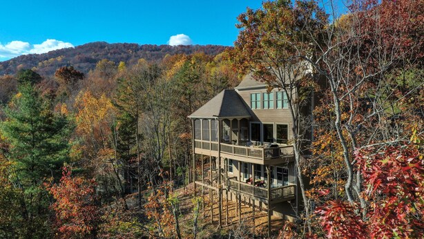 Une cabane en bois à deux étages, dotée d’un balcon, entourée d’un feuillage automnal et avec une chaîne de montagnes en arrière-plan.