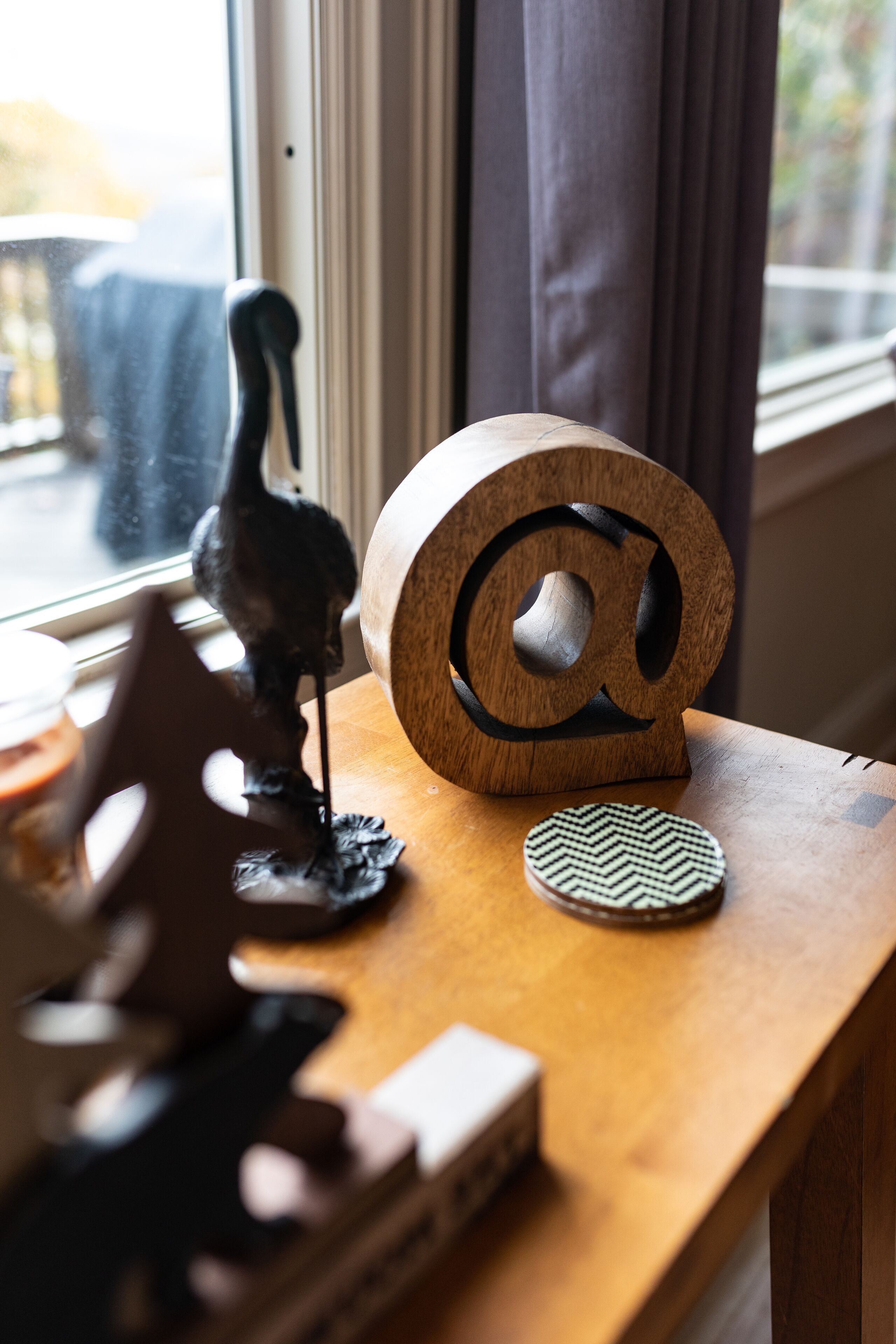 Een houten tafel met een houten @-symbool, een klein beeldje en een decoratieve onderzetter.