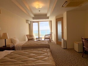 A hotel room with two beds, a small table, two chairs, a lamp, and a view of the outdoors.