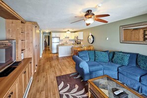 Un salon avec un canapé bleu, des meubles en bois, un téléviseur et un ventilateur de plafond.